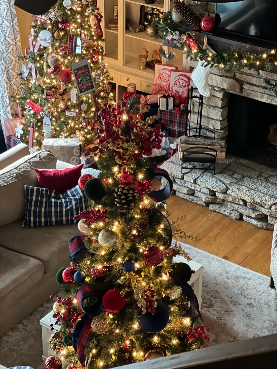 An elevated view of a high-ceilinged living room arranged with several Christmas trees and glowing garland.