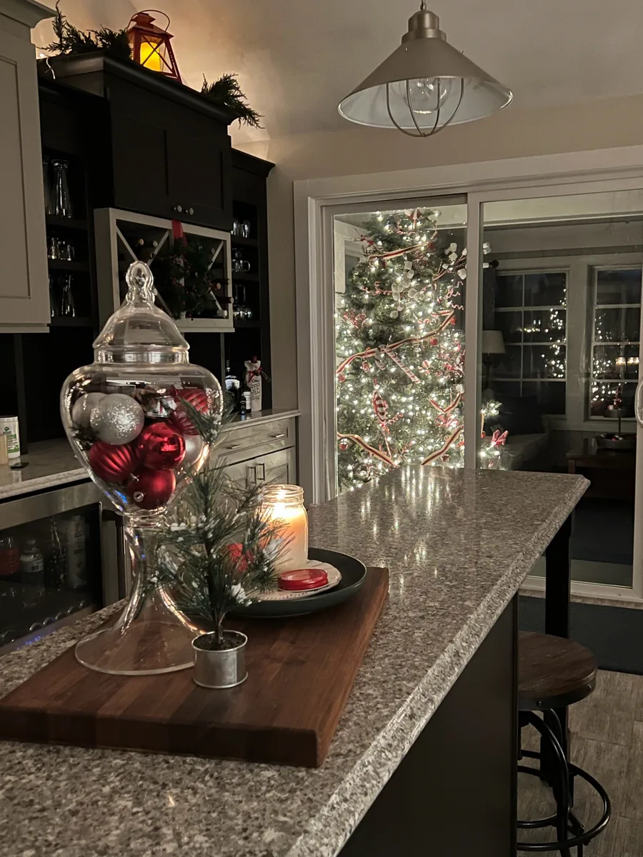 A festive red-and-white Christmas tree glows through a kitchen doorway.
